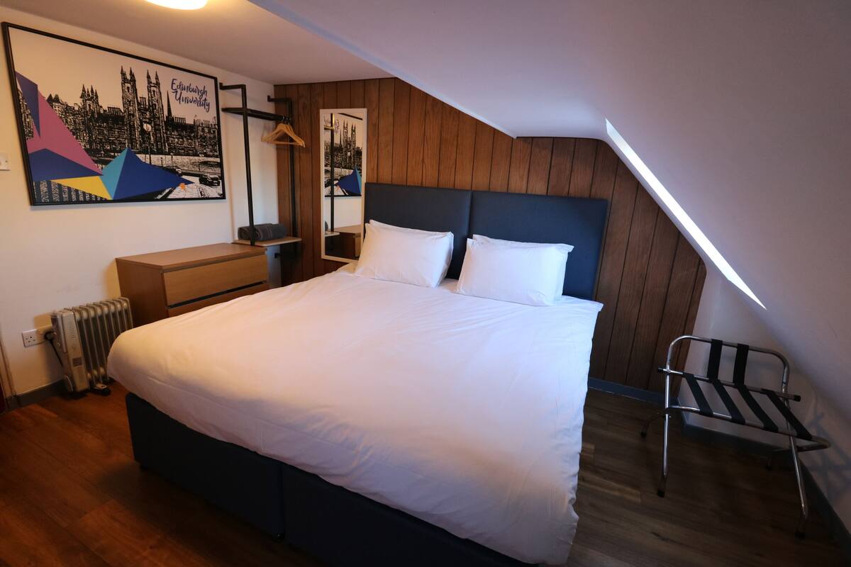 A bedroom with a large bed, wooden panel walls, a radiator, a chair, and a framed picture on the wall.