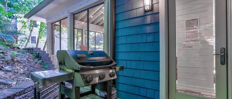 An outdoor grill setup near a house with blue siding and a white door.