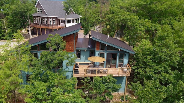 A two-story house with a balcony, surrounded by dense forest.
