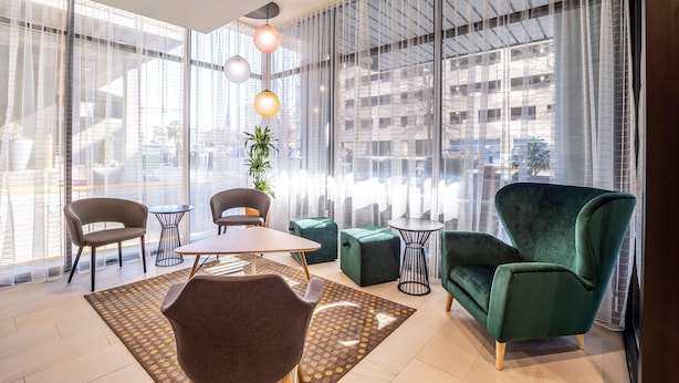 A modern room with large windows, a green armchair, a brown chair, a small round table, and a potted plant. - Holiday Inn Columbia - Downtown by IHG (Columbia)