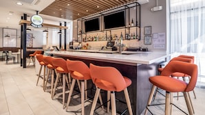 A modern bar area with a sign reading "TOAST ORDER HERE," bar stools, a counter with a laptop, and a display of liquor bottles. - Holiday Inn Columbia - Downtown by IHG (Columbia)