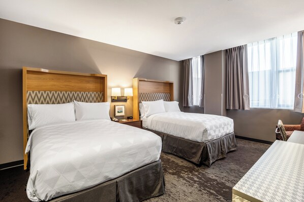 A hotel room with two beds, a small table, a chair, a nightstand with lamps, and a window with curtains. - Holiday Inn Columbia - Downtown by IHG (Columbia)