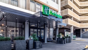 A modern hotel entrance with a green sign, outdoor seating, and planters. - Holiday Inn Columbia - Downtown by IHG (Columbia)