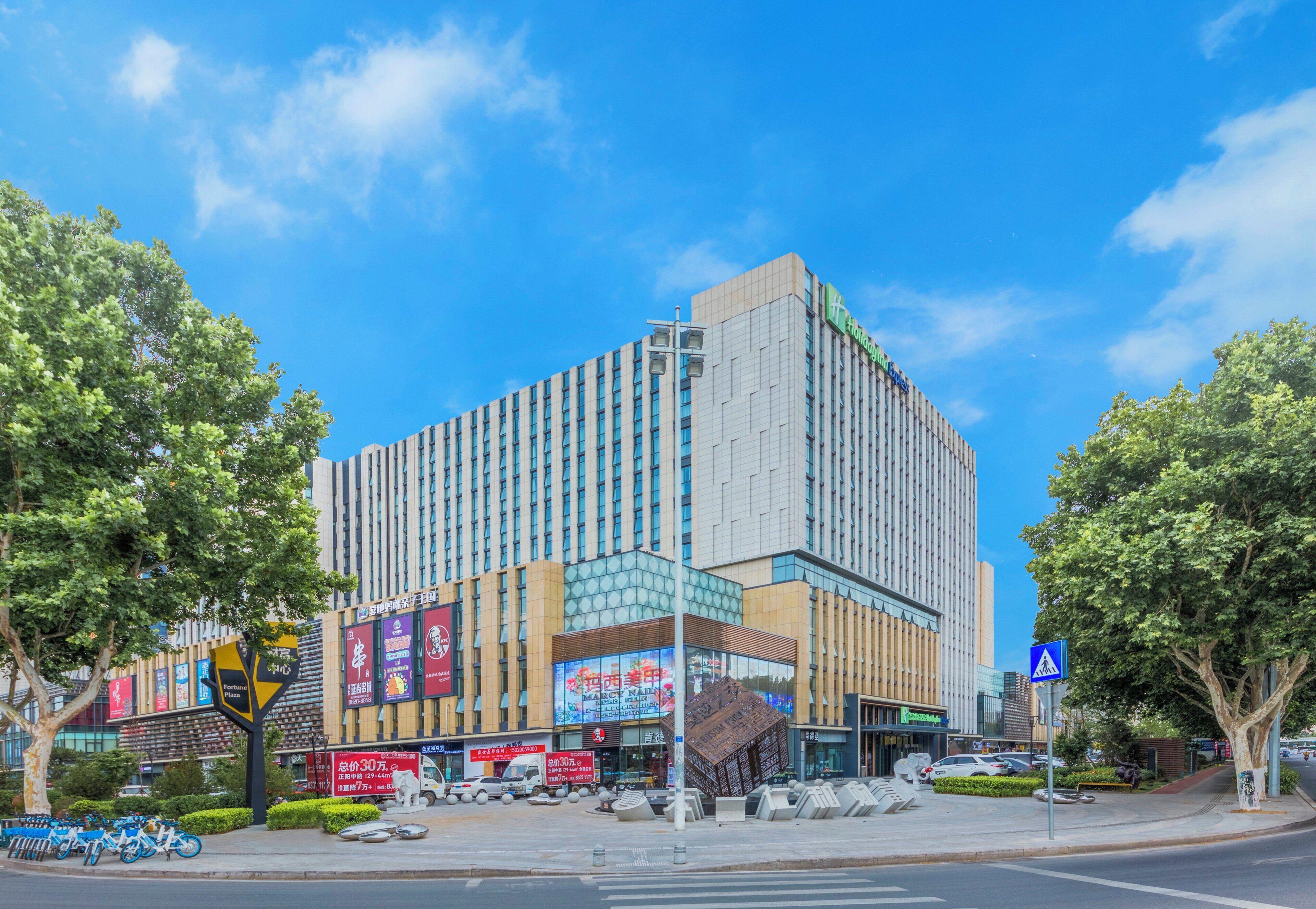 A multi-story hotel with a modern facade, located at a street corner with trees and a pedestrian crossing.
