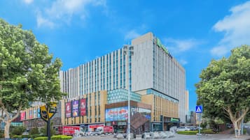 A multi-story hotel with a modern facade, located at a street corner with trees and a pedestrian crossing.