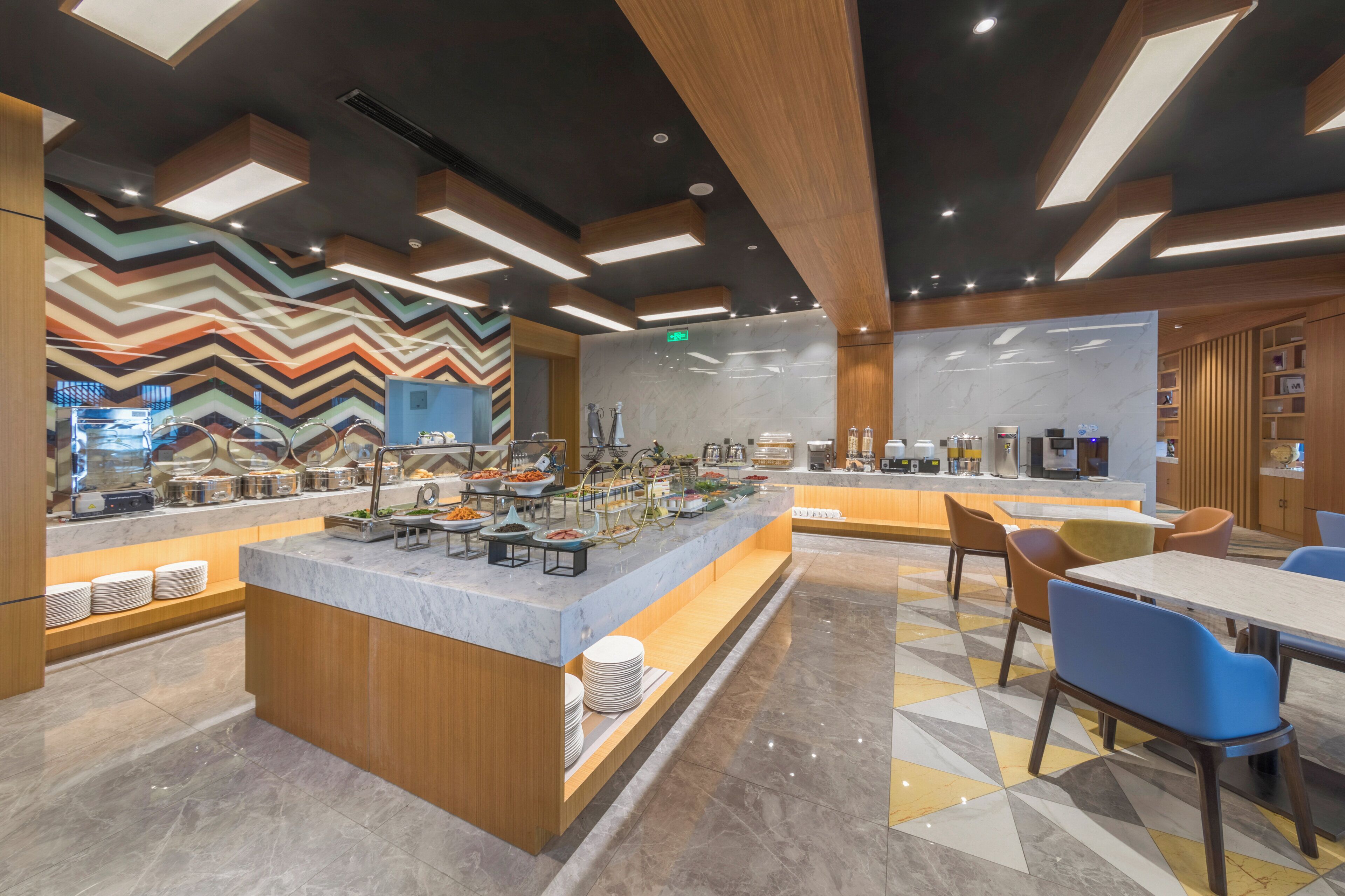 Un moderno comedor para el desayuno con una isla central, bufé con diversas opciones de comida y diferentes disposiciones de asientos.