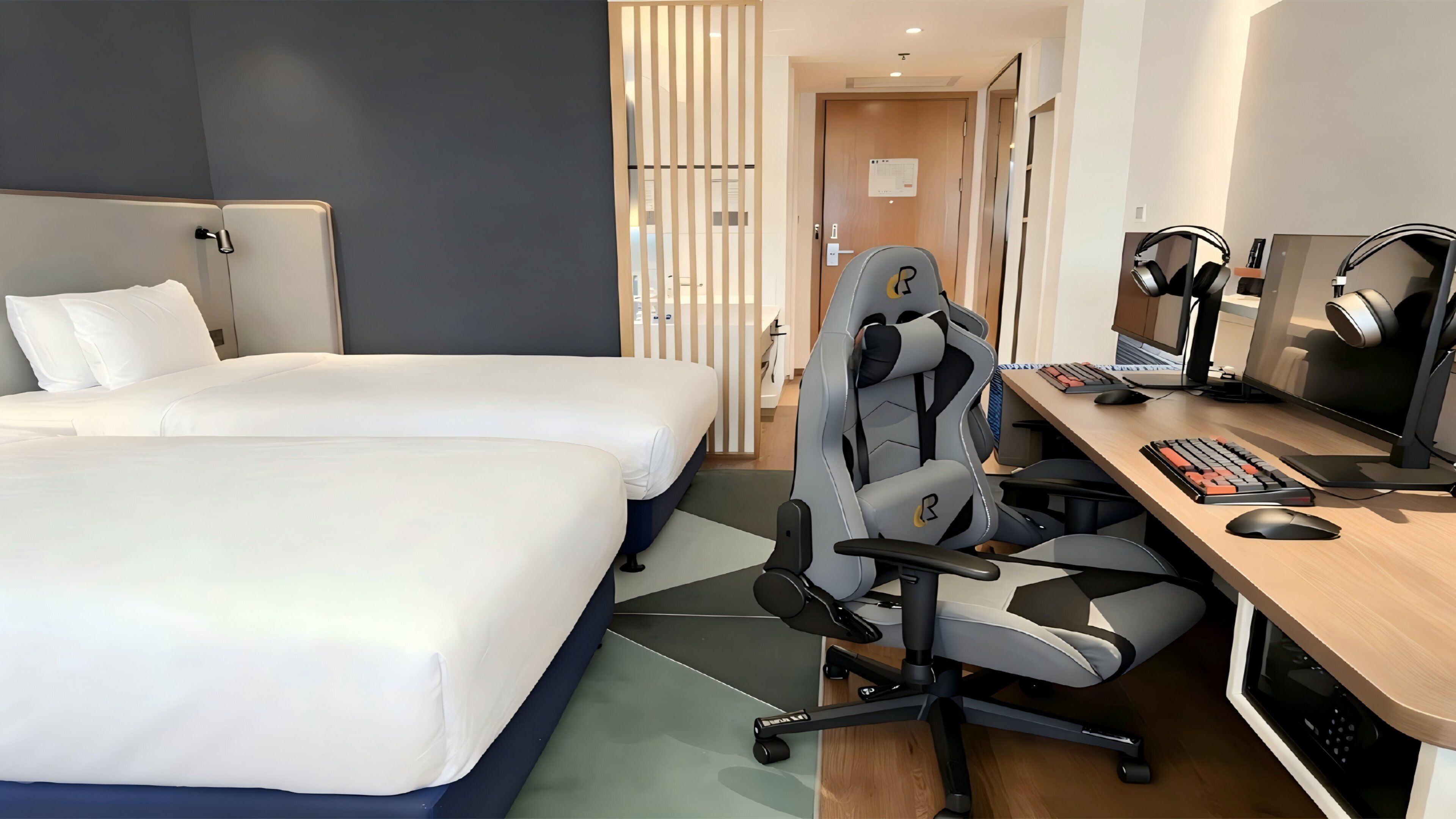 Une chambre d’hôtel avec deux lits, un bureau équipé d’un ordinateur et une chaise moderne.