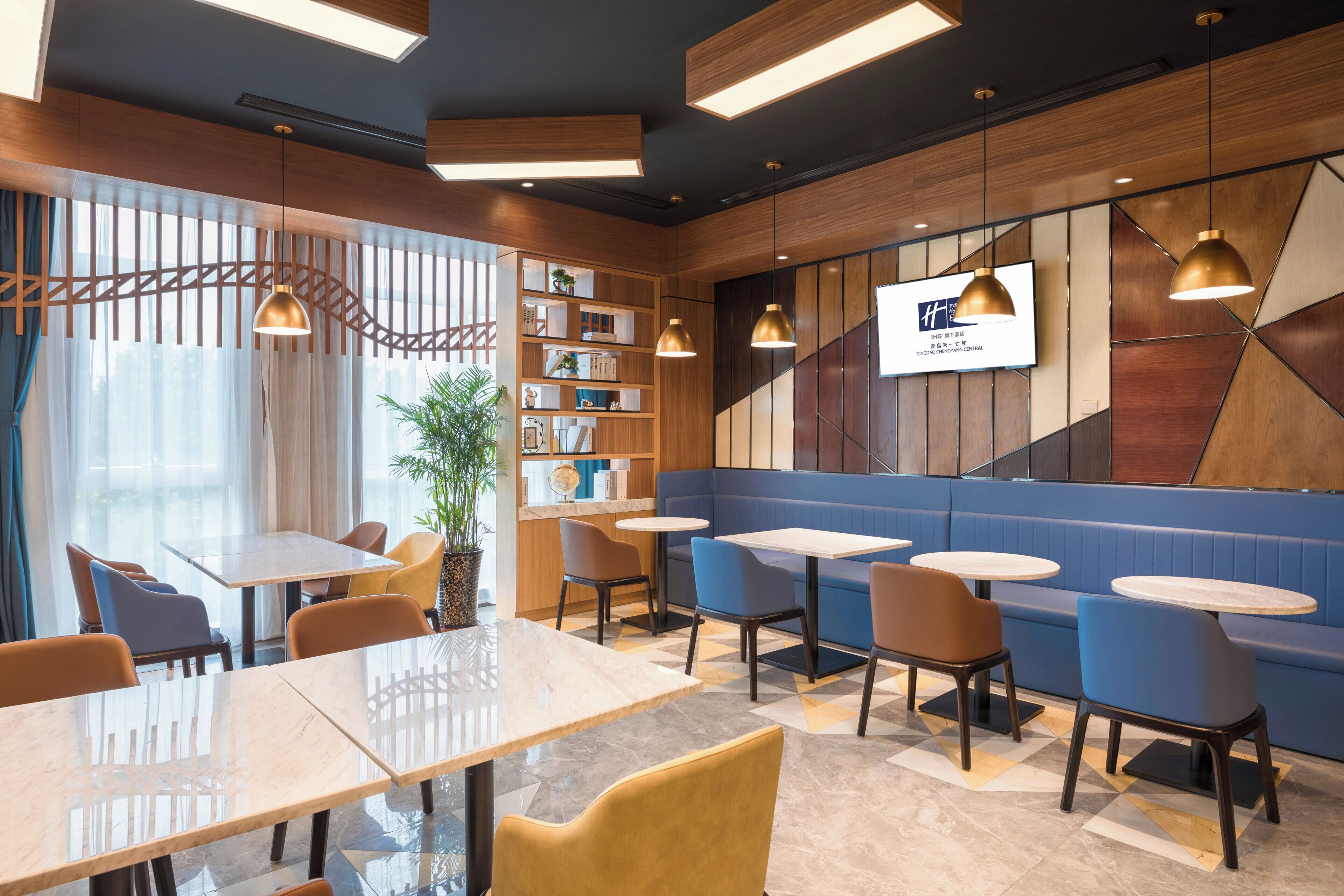 A modern interior with tables and chairs, a bookshelf, and a TV screen.
