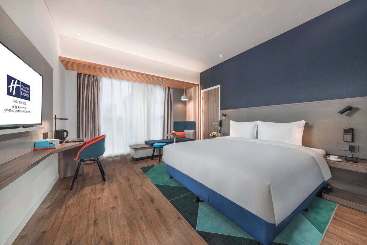 A modern hotel room with a large bed, a desk, a chair, and a television.