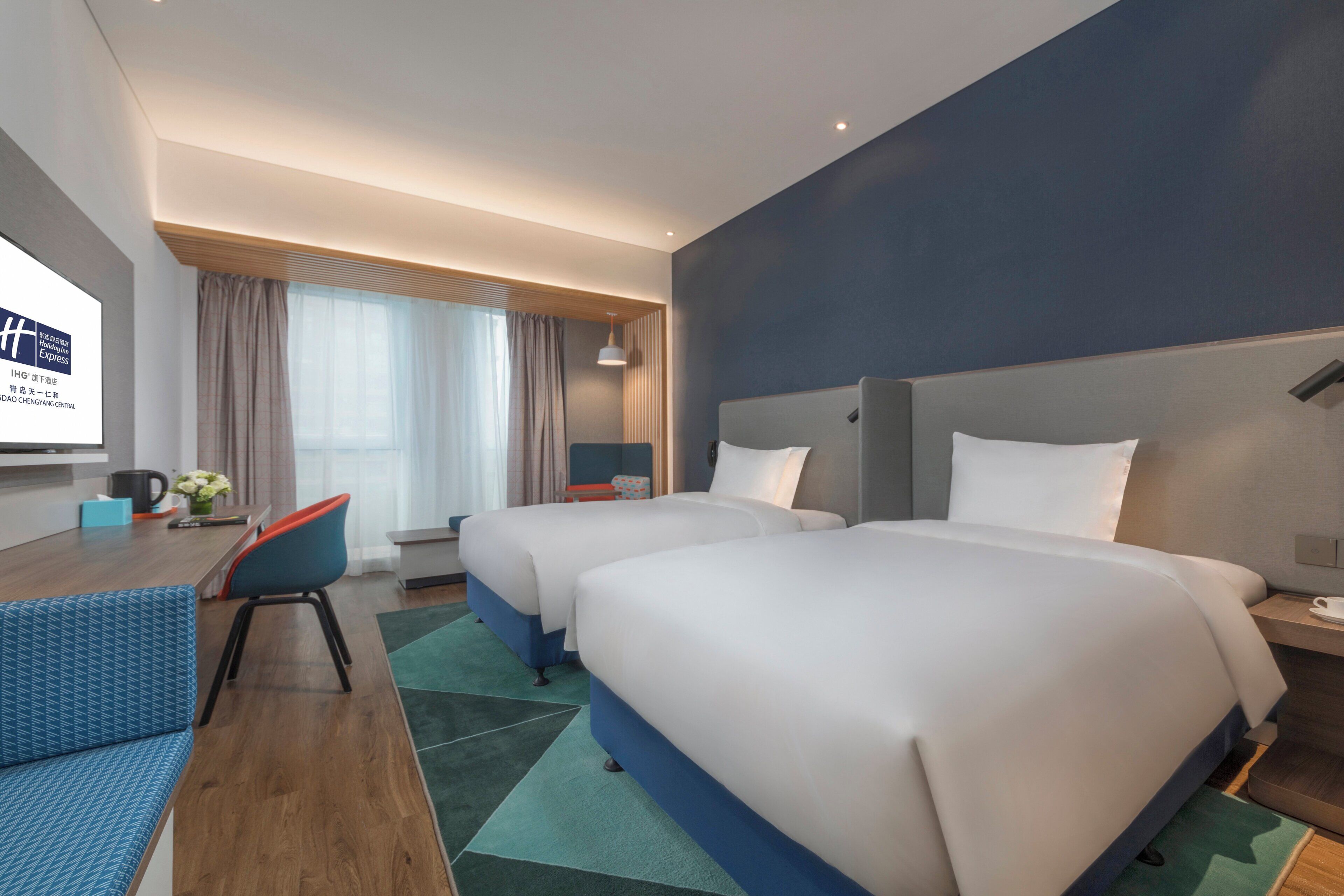 A hotel room with two beds, a desk, a chair, and a TV.