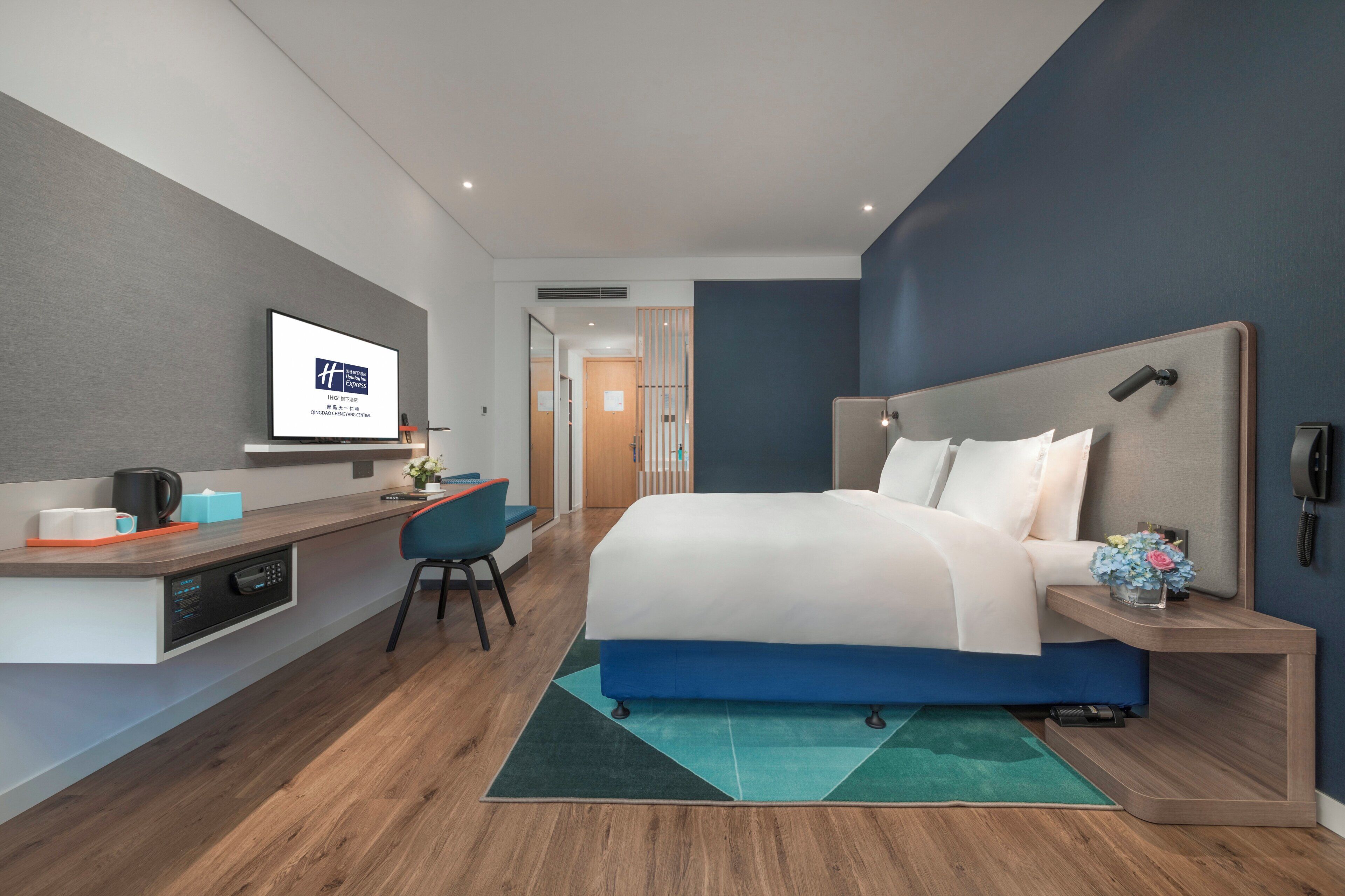Una habitación de hotel moderna con cama, escritorio, silla y televisor mostrando el nombre del hotel.