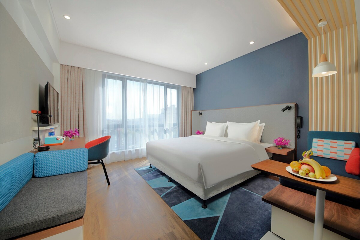 A modern hotel room with a large bed, a desk, a chair, and a television.