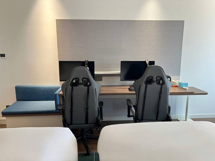 A hotel room with a desk, two monitors, a blue sofa, and two chairs.