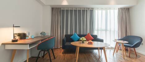 A modern living room with a sofa, two chairs, a coffee table, a desk, and a large window with curtains.