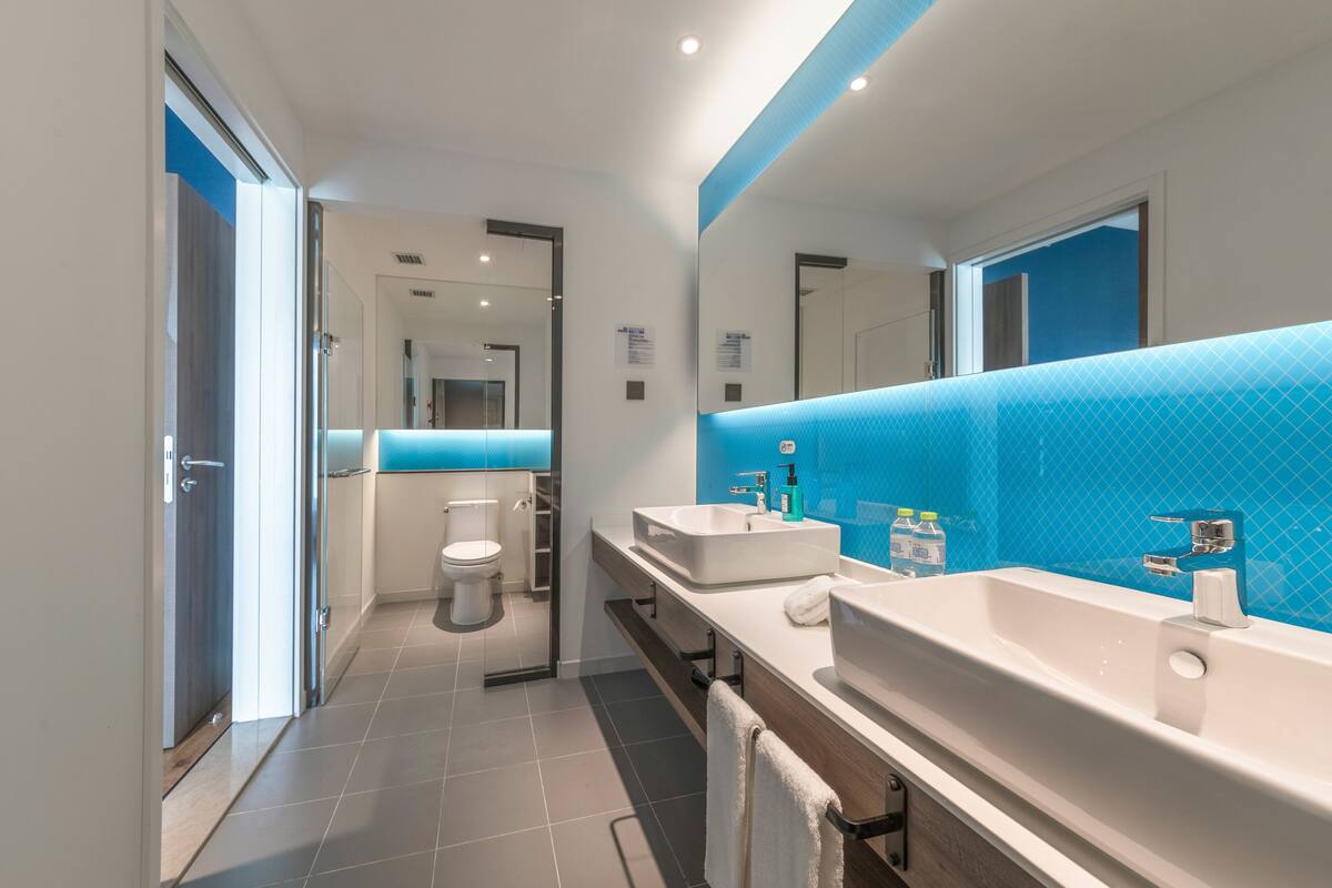 Ein modernes Badezimmer mit einem großen Spiegel, zwei Waschbecken und einer Toilette.