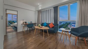 A modern living room with a sofa, chairs, a dining table, and a view of a cityscape through large windows.