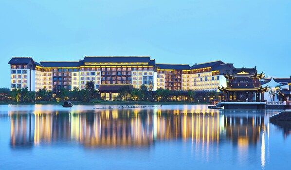 Um hotel grande com vários edifícios, uma superfície aquática refletora à frente e elementos arquitetônicos tradicionais.