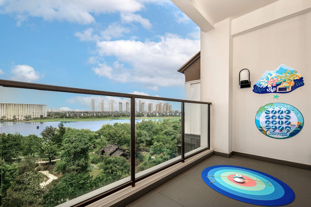 Ein Balkon mit Blick auf einen See und eine Stadtlandschaft, eine Wandleuchte und ein dekoratives, rundes Kunstwerk.