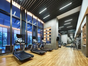 Uma academia moderna com esteiras, aparelhos de musculação e amplas janelas que oferecem vista para o exterior.