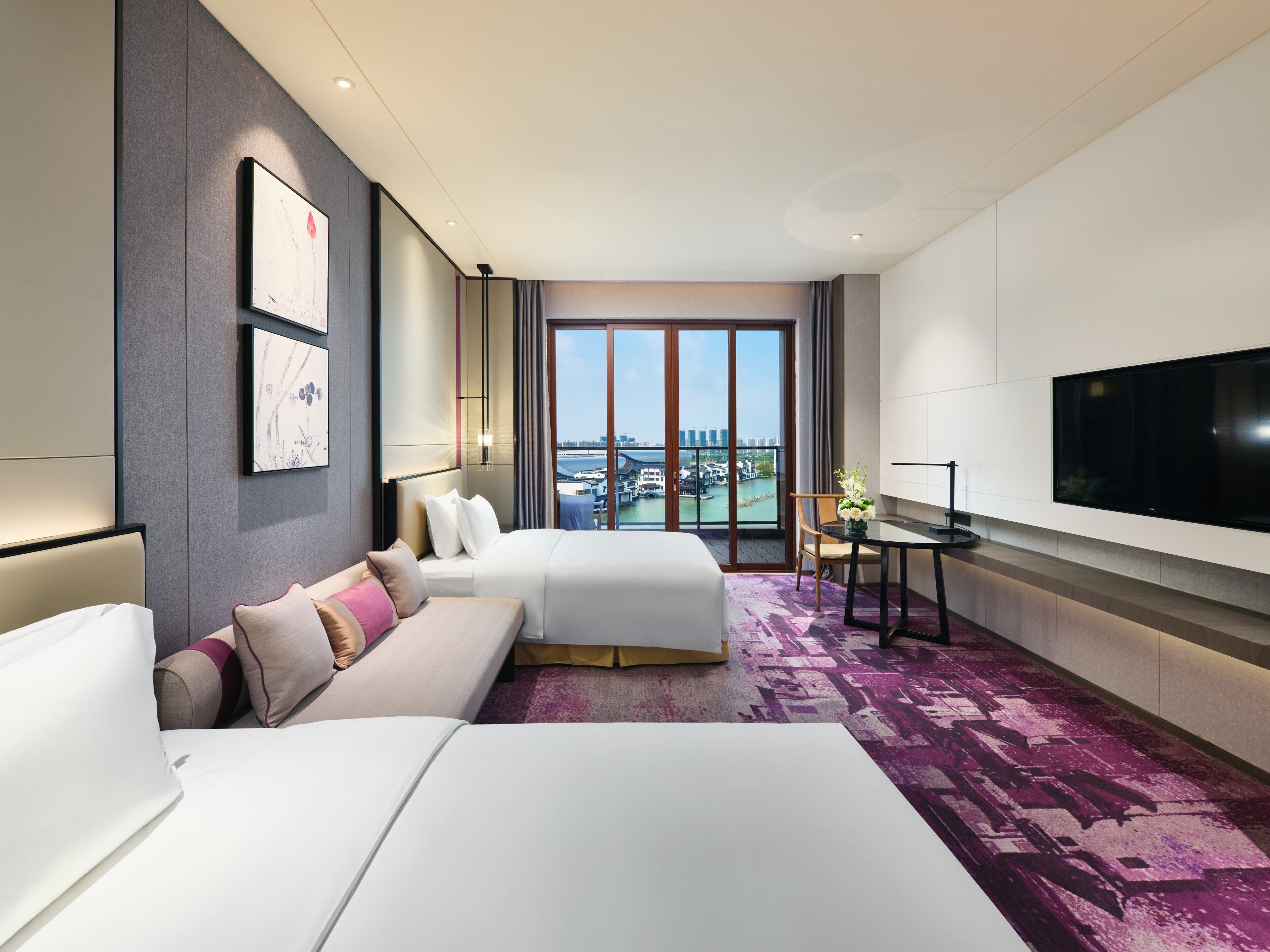 A hotel room with a large bed, a smaller bed, a desk, a TV, and a view of a cityscape.