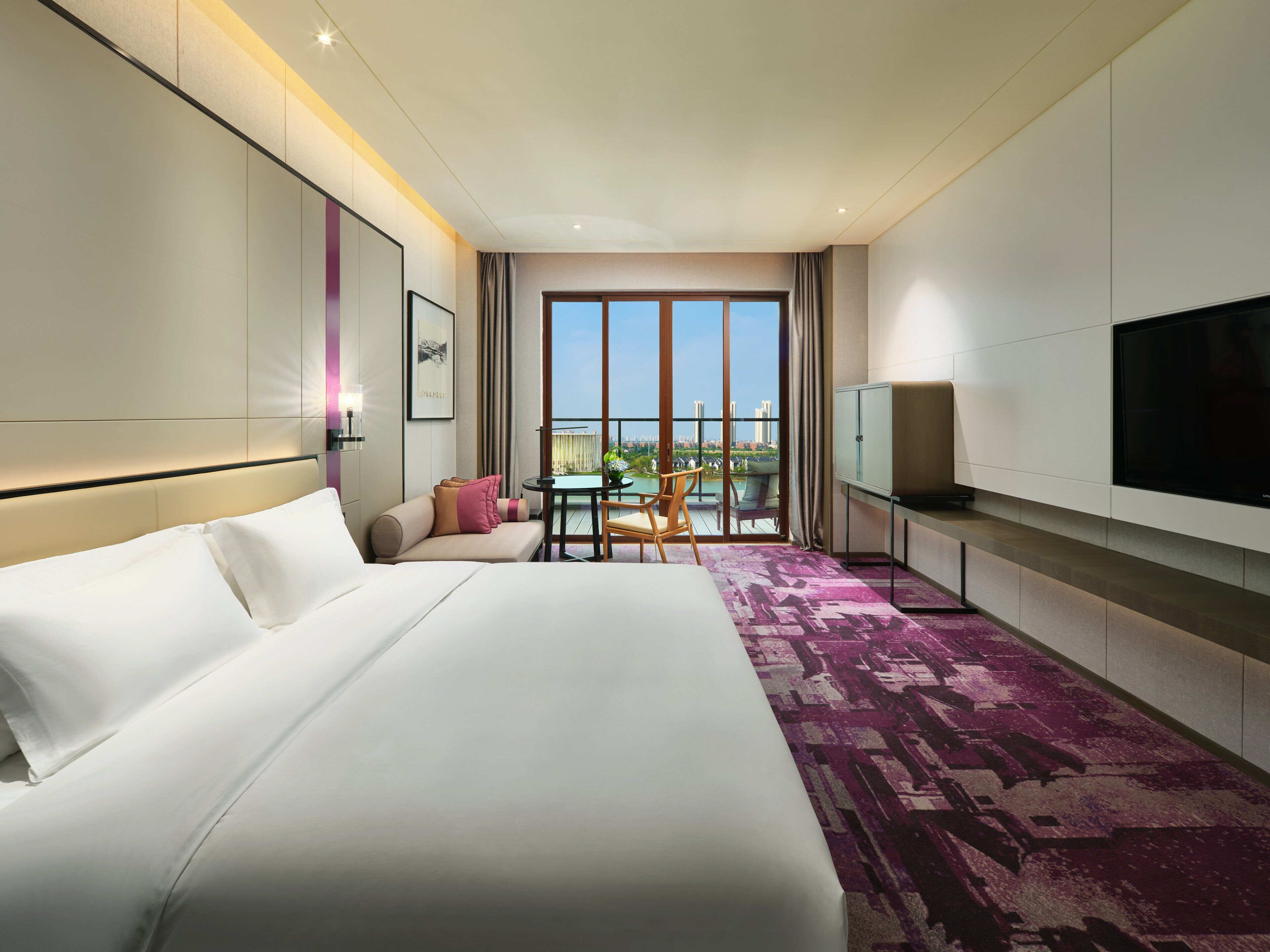 Una habitación de hotel con una cama grande, televisor, balcón con vistas y zona de comedor.
