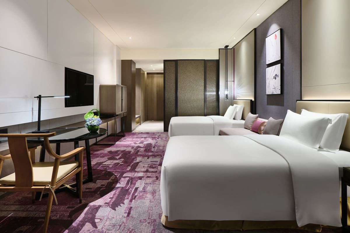 Ein modernes Hotelzimmer mit einem großen Bett, einem Schreibtisch mit Stuhl, einem Flachbildfernseher und einer dekorativen Vase.