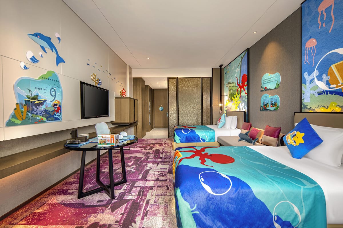 Ein Hotelzimmer mit zwei Betten, einem Fernseher, einem kleinen Tisch und Bildern an den Wänden.