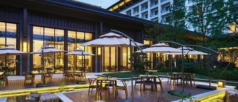 An outdoor patio area with tables and umbrellas, a koi pond, and a building with large windows.