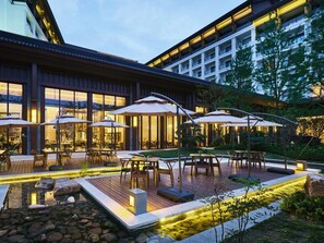 An outdoor patio area with tables and umbrellas, a koi pond, and a building with large windows. - Crowne Plaza Wuxi Lake View by IHG (Wuxi)