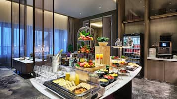 A buffet with various food items, a coffee machine, and a refrigerator.