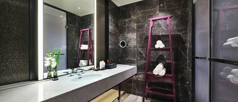 A modern bathroom with a marble vanity, a large mirror, a pink ladder shelf, and a marble wall.