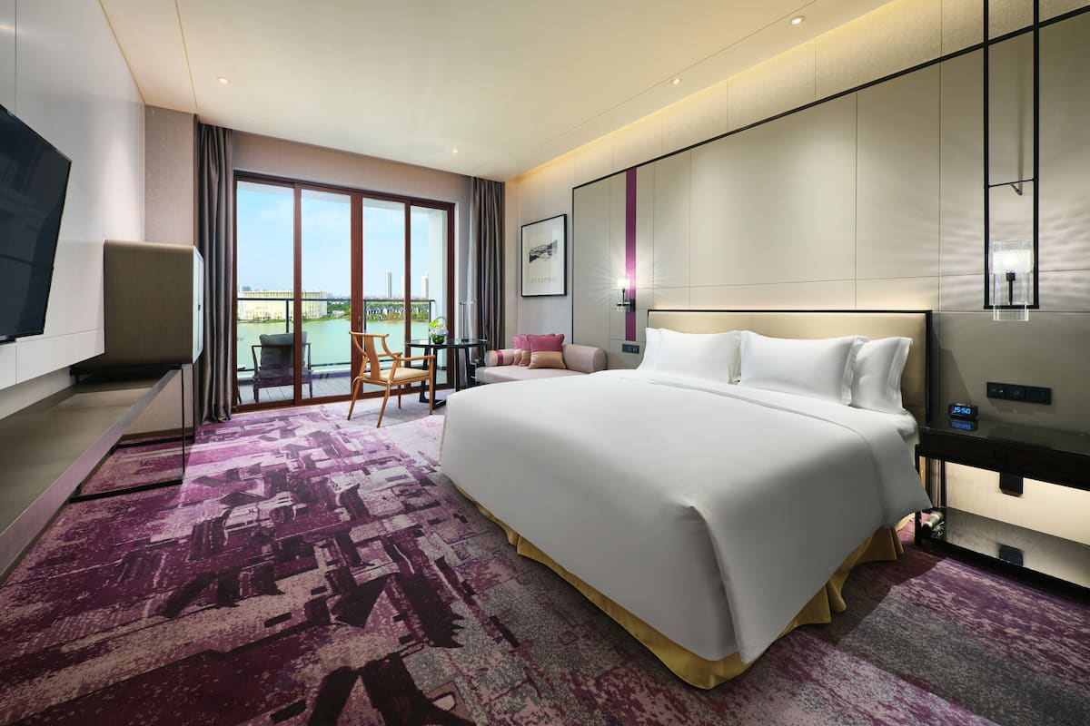 Ein modernes Hotelzimmer mit einem großen Bett, einem Fernseher, einem Schreibtisch und einem Balkon mit Blick auf die Stadt.