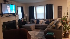 A living room with a fireplace, a sofa, a TV, and a potted plant. - Spacious 5 Bedroom rental (Waukesha)