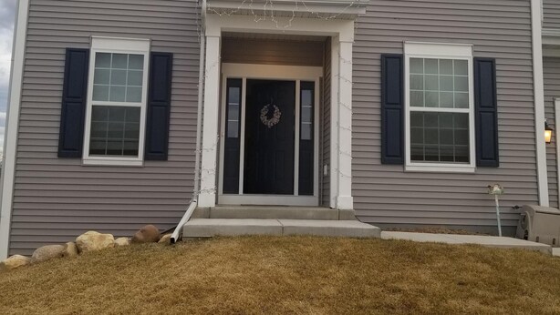A two-story house with a front porch, a wreath on the door, and a small garden area in front. - Spacious 5 Bedroom rental (Waukesha)
