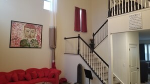A living room with a red sofa, a painting, a staircase, and a sign on the wall. - Spacious 5 Bedroom rental (Waukesha)