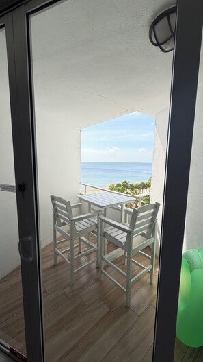 A balcony with a table and chairs, overlooking a beach and ocean.