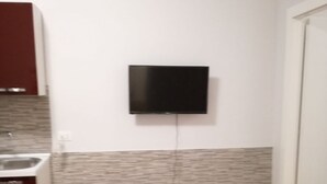 Una piccola cucina moderna con una TV a schermo piatto montata a parete, un tavolo da pranzo con una sedia e una tovaglia rossa.
