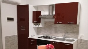 Una cucina compatta con un tavolo bianco, tovagliette rosse, un vaso con fiori e una sedia verde.