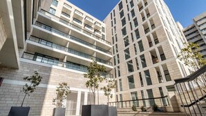 A modern multi-story building with balconies, large windows, and a paved courtyard with planters. - Cosy 1 bedroom city center (Jerusalem)