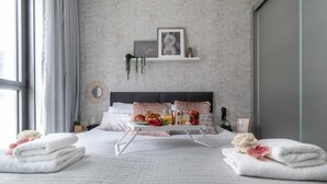 A neatly made bed with a tray of breakfast items, a bedside table with a lamp, and a wall-mounted shelf with decorative items. - Cosy 1 bedroom city center (Jerusalem)