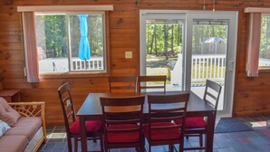 L’intérieur d’un chalet en bois comprend une table et des chaises, un canapé et une vue sur le jardin à travers une porte-fenêtre coulissante.