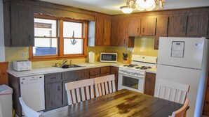 Une cuisine avec des meubles de rangement en bois, un réfrigérateur blanc, un four à micro-ondes, une cuisinière et une table à manger avec des chaises.