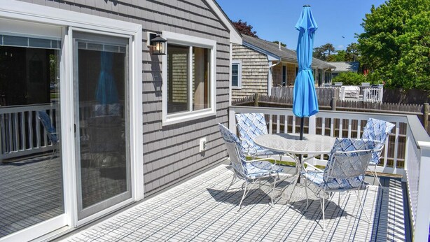 Une terrasse extérieure couverte, avec une table et des chaises, un parasol bleu et une porte-fenêtre coulissante.