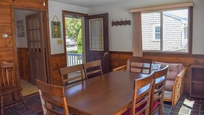 Un coin repas en bois, avec une table et des chaises, un banc et une fenêtre donnant sur une maison.