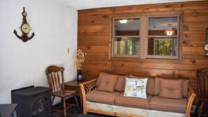 Une pièce chaleureuse avec un mur en bois, une fenêtre donnant sur un beau paysage, un canapé, un fauteuil, une table et une horloge ancienne.