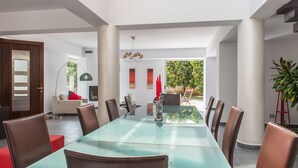 A modern dining area with a glass table, leather chairs, and a view of a garden. - Casa Di Verde Villa (Platanias)