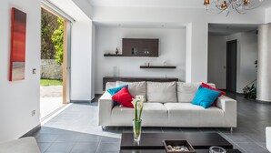 A modern living room with a white sofa, red and blue cushions, a glass vase with flowers, and a chandelier. - Casa Di Verde Villa (Platanias)