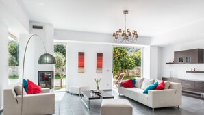A modern living room with two sofas, a coffee table, and a floor lamp. There is a fireplace and a view of greenery outside. - Casa Di Verde Villa (Platanias)