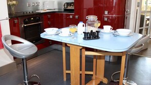 A modern kitchen with red cabinets, a blue table, and a breakfast setup including a coffee maker, cups, and a glass of orange juice. - Victorian cottage, large gardens, near river, Hadrian's Wall & Allendale (Allendale)