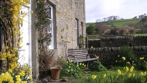 A stone building with a bench in front, surrounded by a garden with yellow flowers. - Victorian cottage, large gardens, near river, Hadrian's Wall & Allendale (Allendale)